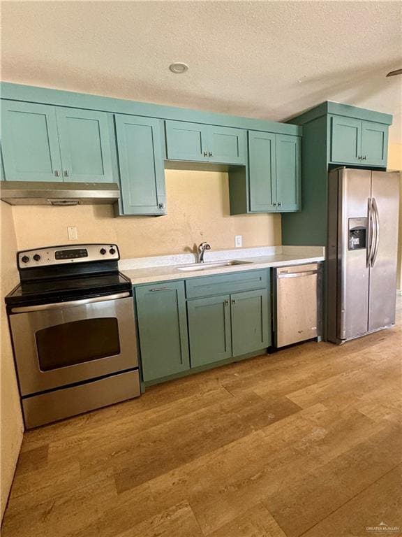 kitchen with light countertops, a textured ceiling, light wood-style flooring, appliances with stainless steel finishes, and green cabinets