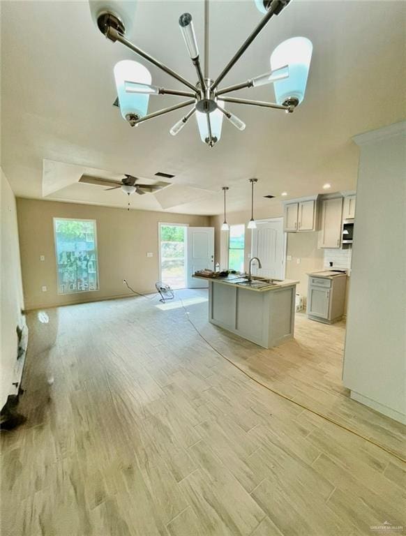 kitchen with light wood-type flooring, backsplash, decorative light fixtures, a center island with sink, and white cabinetry