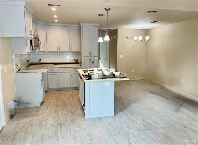 kitchen featuring white cabinetry, light hardwood / wood-style flooring, backsplash, decorative light fixtures, and a kitchen island with sink