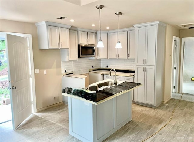 kitchen with decorative backsplash, a kitchen island with sink, sink, pendant lighting, and white cabinetry