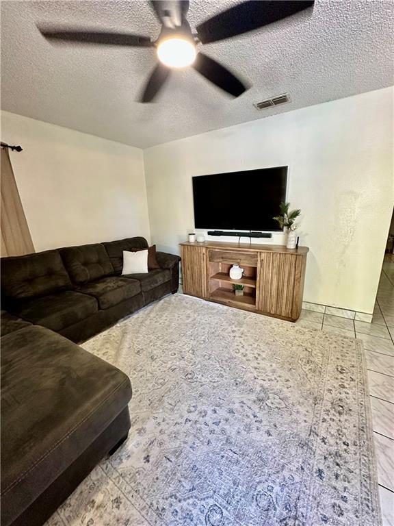 living area featuring ceiling fan, visible vents, and a textured ceiling