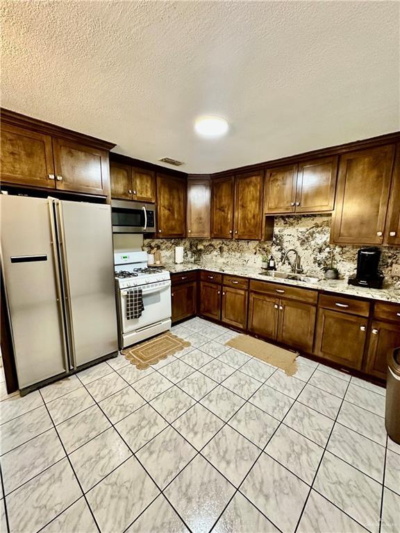 kitchen with visible vents, white gas stove, freestanding refrigerator, a sink, and stainless steel microwave