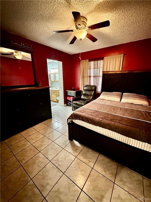 bedroom with light tile patterned flooring, a ceiling fan, ensuite bathroom, and a textured ceiling