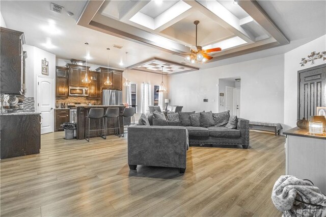 living room with ceiling fan, visible vents, coffered ceiling, and light wood finished floors