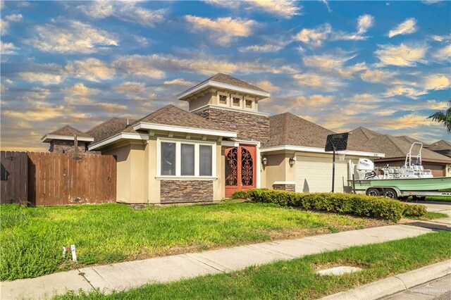 view of front of home with stucco siding, fence, stone siding, a garage, and a yard