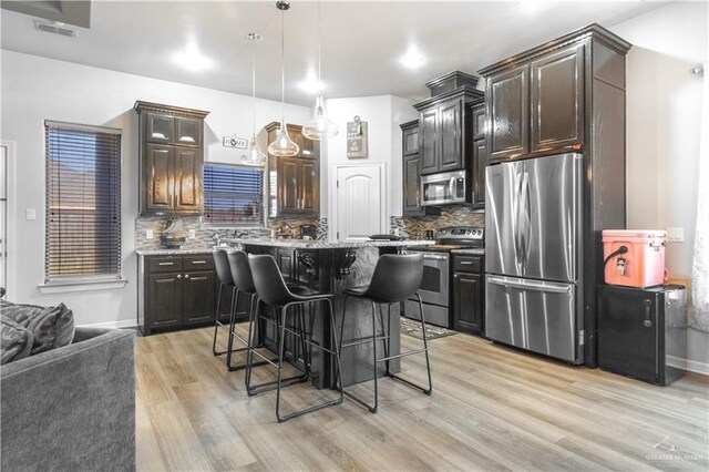 kitchen featuring backsplash, a breakfast bar area, stainless steel appliances, light wood-style floors, and dark brown cabinets