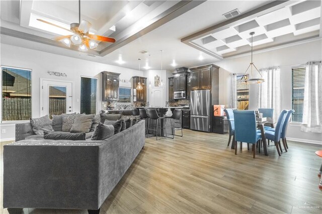 living area featuring a tray ceiling, visible vents, light wood-style flooring, and ceiling fan