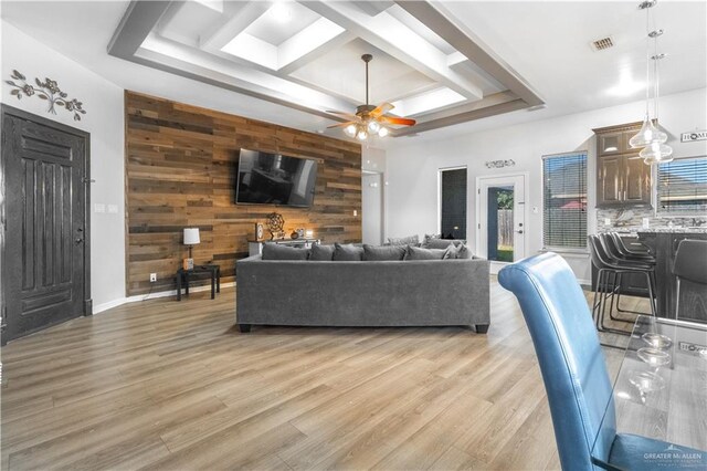 living area with visible vents, wood walls, light wood-type flooring, an accent wall, and coffered ceiling