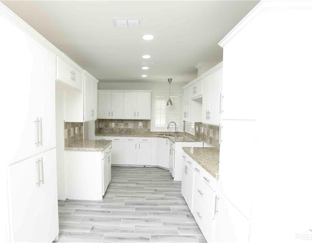 kitchen featuring white cabinetry, sink, backsplash, decorative light fixtures, and light wood-type flooring