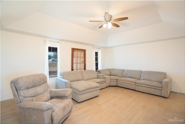 living room featuring a raised ceiling, ceiling fan, and light hardwood / wood-style flooring