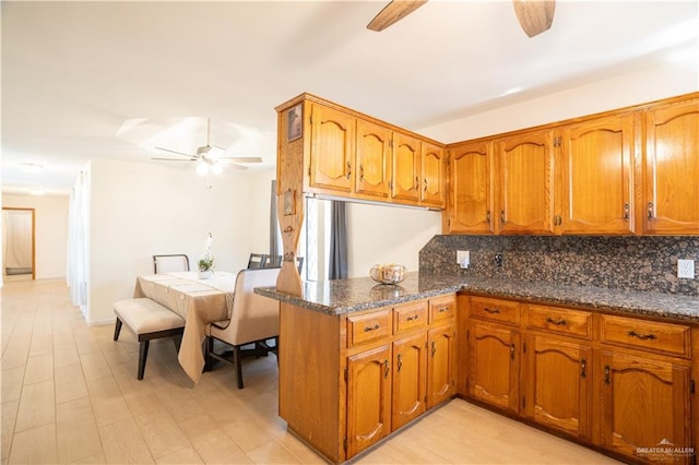 kitchen with dark stone counters, light wood-type flooring, decorative backsplash, and kitchen peninsula