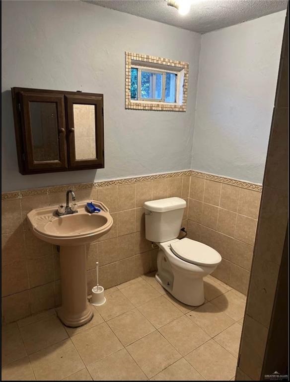 bathroom with a textured ceiling, tile patterned floors, tile walls, and toilet