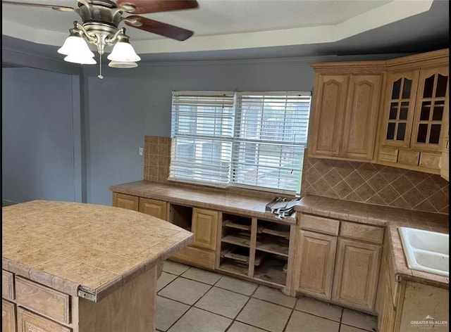 kitchen featuring ceiling fan, sink, a raised ceiling, decorative backsplash, and light tile patterned floors