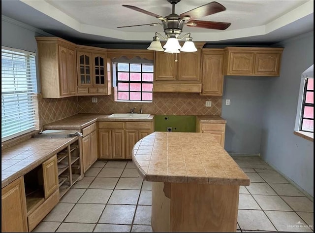 kitchen featuring a tray ceiling, sink, a kitchen island, and light tile patterned flooring