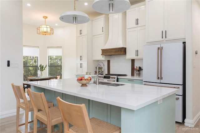 kitchen featuring light countertops, tasteful backsplash, a center island with sink, freestanding refrigerator, and custom exhaust hood