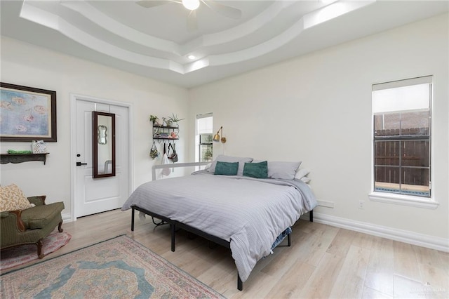 bedroom with a ceiling fan, a tray ceiling, baseboards, and light wood finished floors