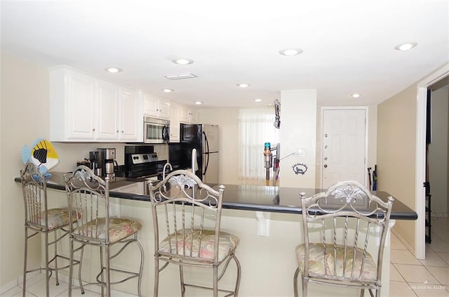 3400 Gulf Blvd Unit 403, South Padre Island, TX 78597 - kitchen with stainless steel appliances, dark countertops, a peninsula, light tile patterned flooring, and a breakfast bar
