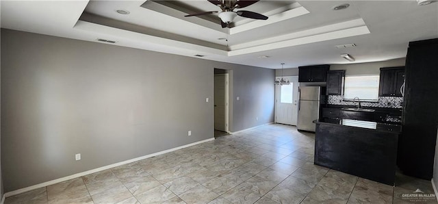 kitchen featuring stainless steel fridge, a raised ceiling, ceiling fan, and sink