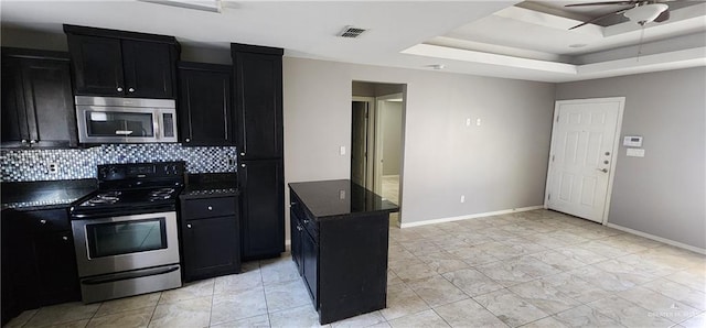 kitchen with backsplash, ceiling fan, stainless steel appliances, and a tray ceiling