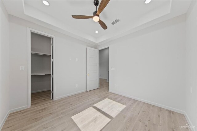 unfurnished bedroom featuring a raised ceiling, a spacious closet, and ceiling fan