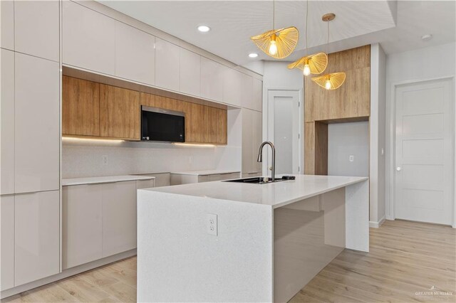 kitchen with sink, decorative light fixtures, a center island with sink, white cabinets, and light hardwood / wood-style floors