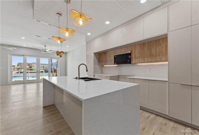 kitchen featuring french doors, sink, a water view, hanging light fixtures, and an island with sink