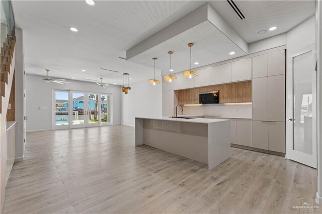 kitchen featuring ceiling fan, sink, pendant lighting, a center island with sink, and white cabinets