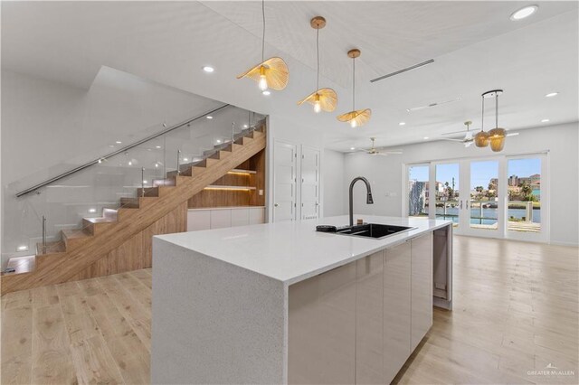 kitchen with ceiling fan, sink, a large island with sink, decorative light fixtures, and white cabinetry