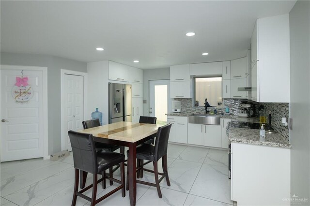 kitchen featuring sink, stainless steel fridge with ice dispenser, light stone counters, decorative backsplash, and white cabinets