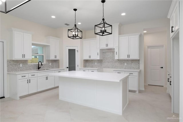 kitchen featuring tasteful backsplash, white cabinets, a kitchen island, decorative light fixtures, and a sink