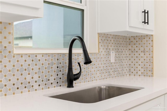 kitchen with white cabinets, light countertops, a sink, and decorative backsplash