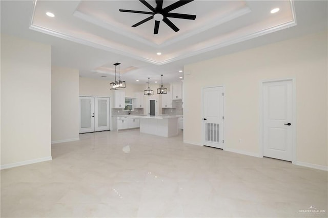 unfurnished living room with baseboards, a tray ceiling, a ceiling fan, and ornamental molding