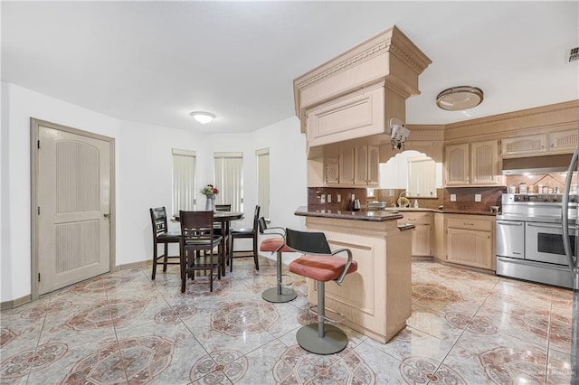 kitchen with sink, backsplash, stainless steel range with electric stovetop, light brown cabinetry, and a breakfast bar