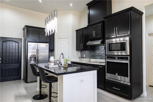 kitchen with under cabinet range hood, a sink, tasteful backsplash, appliances with stainless steel finishes, and dark cabinets