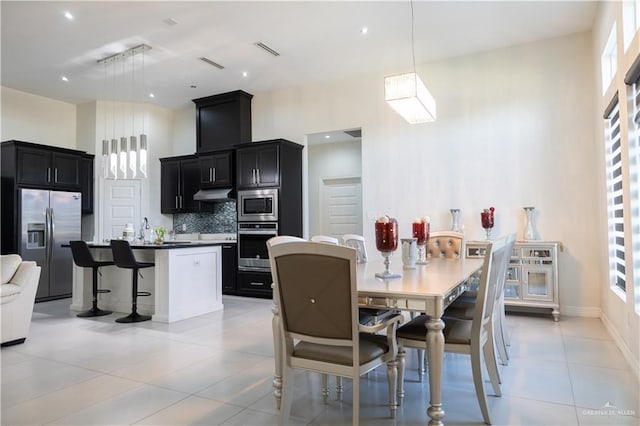 dining area featuring light tile patterned floors, baseboards, visible vents, and a towering ceiling