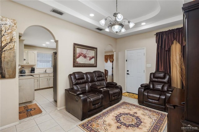 living room with light tile patterned floors, sink, a notable chandelier, and a raised ceiling