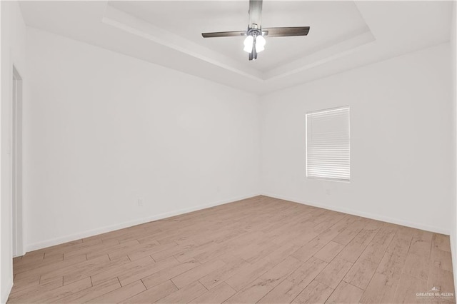 empty room featuring a tray ceiling, light hardwood / wood-style flooring, and ceiling fan