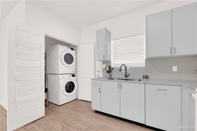 clothes washing area with sink, light hardwood / wood-style floors, and stacked washer and clothes dryer