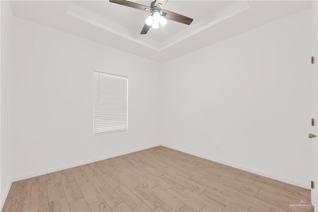 empty room with ceiling fan, light hardwood / wood-style floors, and a tray ceiling