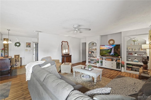 living room featuring built in features, wood finished floors, visible vents, and a textured ceiling