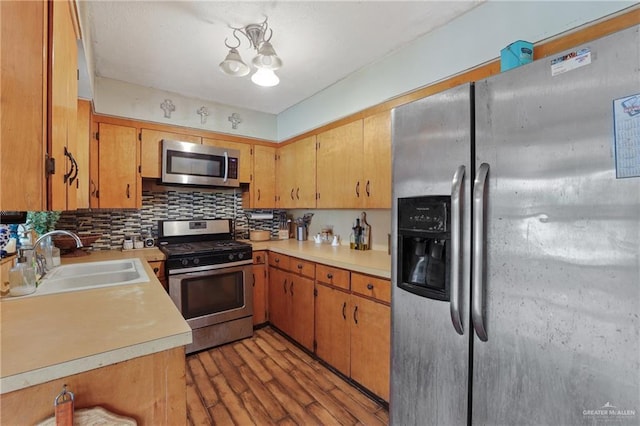 kitchen featuring light wood-type flooring, a sink, backsplash, appliances with stainless steel finishes, and light countertops