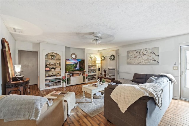 living room with visible vents, a ceiling fan, built in features, a textured ceiling, and wood-type flooring