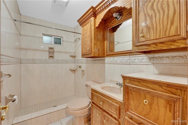 bathroom with tile patterned floors, vanity, tiled shower, tile walls, and toilet