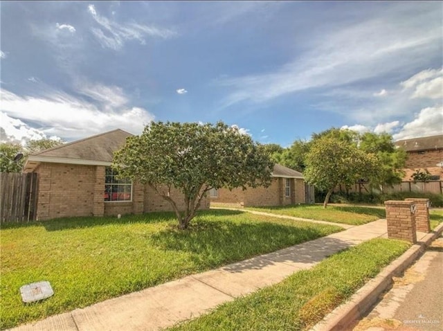 exterior space featuring brick siding, fence, and a yard