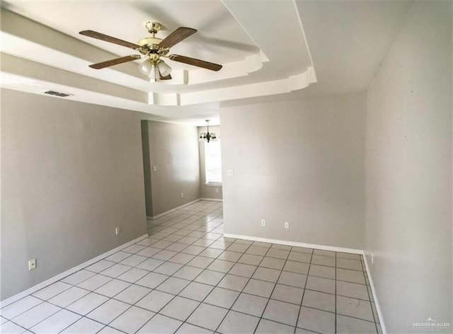 empty room featuring light tile patterned floors, ceiling fan with notable chandelier, visible vents, baseboards, and a raised ceiling