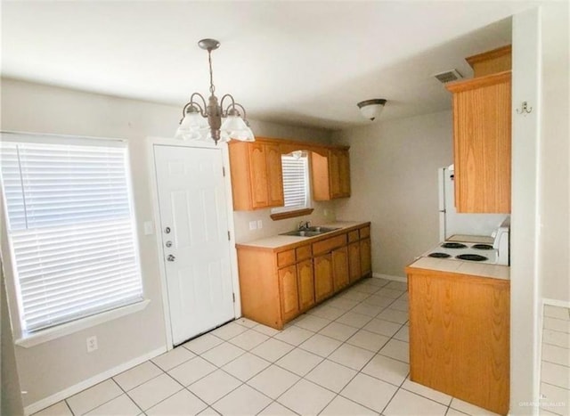 kitchen featuring brown cabinetry, light countertops, a chandelier, pendant lighting, and a sink