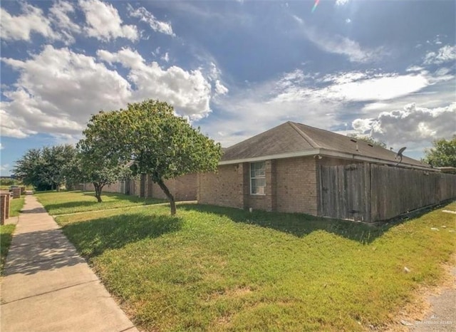 view of side of home with brick siding, a lawn, and fence