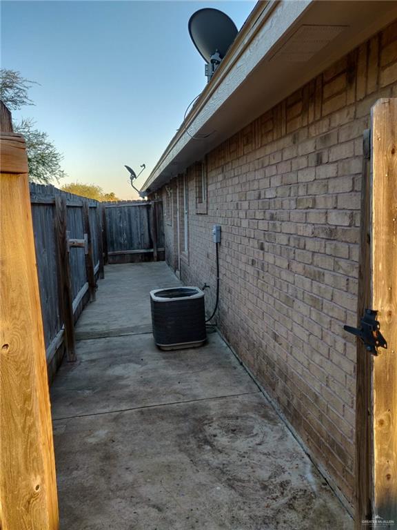 view of home's exterior with central AC, brick siding, a patio area, and fence