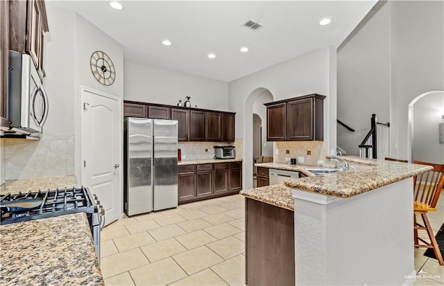 kitchen with a kitchen breakfast bar, tasteful backsplash, light stone counters, kitchen peninsula, and stainless steel appliances