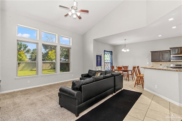 carpeted living room with high vaulted ceiling and ceiling fan with notable chandelier